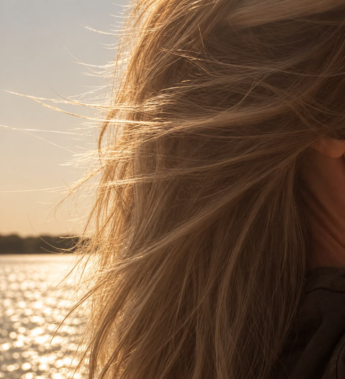 Chevelure blonde soulevée par le vent à contre-jour, plan d’eau scintillant