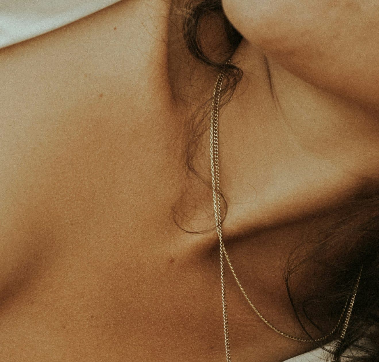 Épaule et clavicule nues en lumière douce, fine chaîne dorée