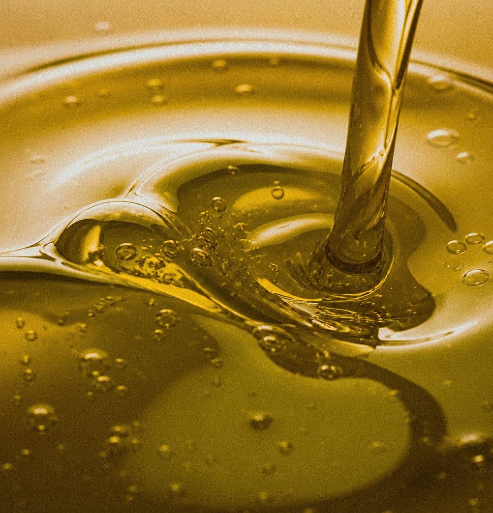 Filet d’huile de chanvre dorée versé en gros plan, bulles en surface